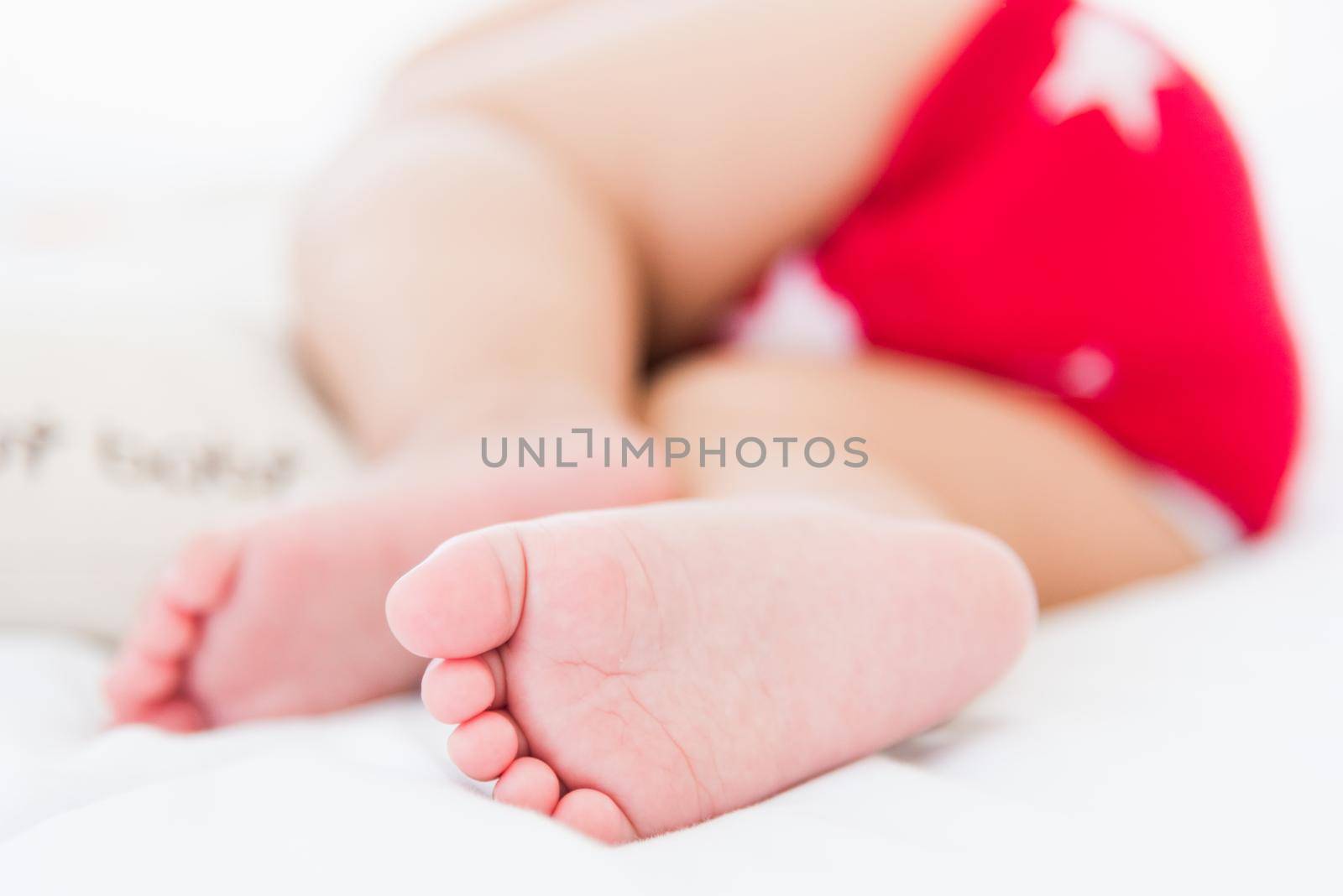 Portrait of beautiful Asian newborn little baby sleeping on white bed at home, Happy baby wears a red shirt relaxing pillow in the room, Family morning at home, close foot