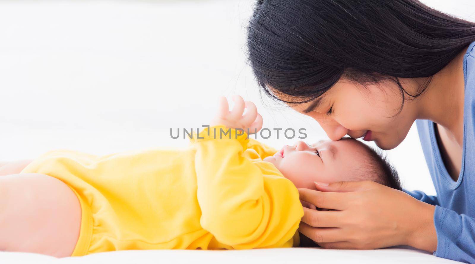 mother kissing her infant newborn baby in a white bed by Sorapop
