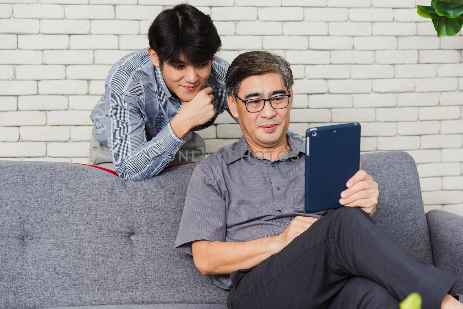 Father man and his son sit on sofa talking chatting on video call by Sorapop