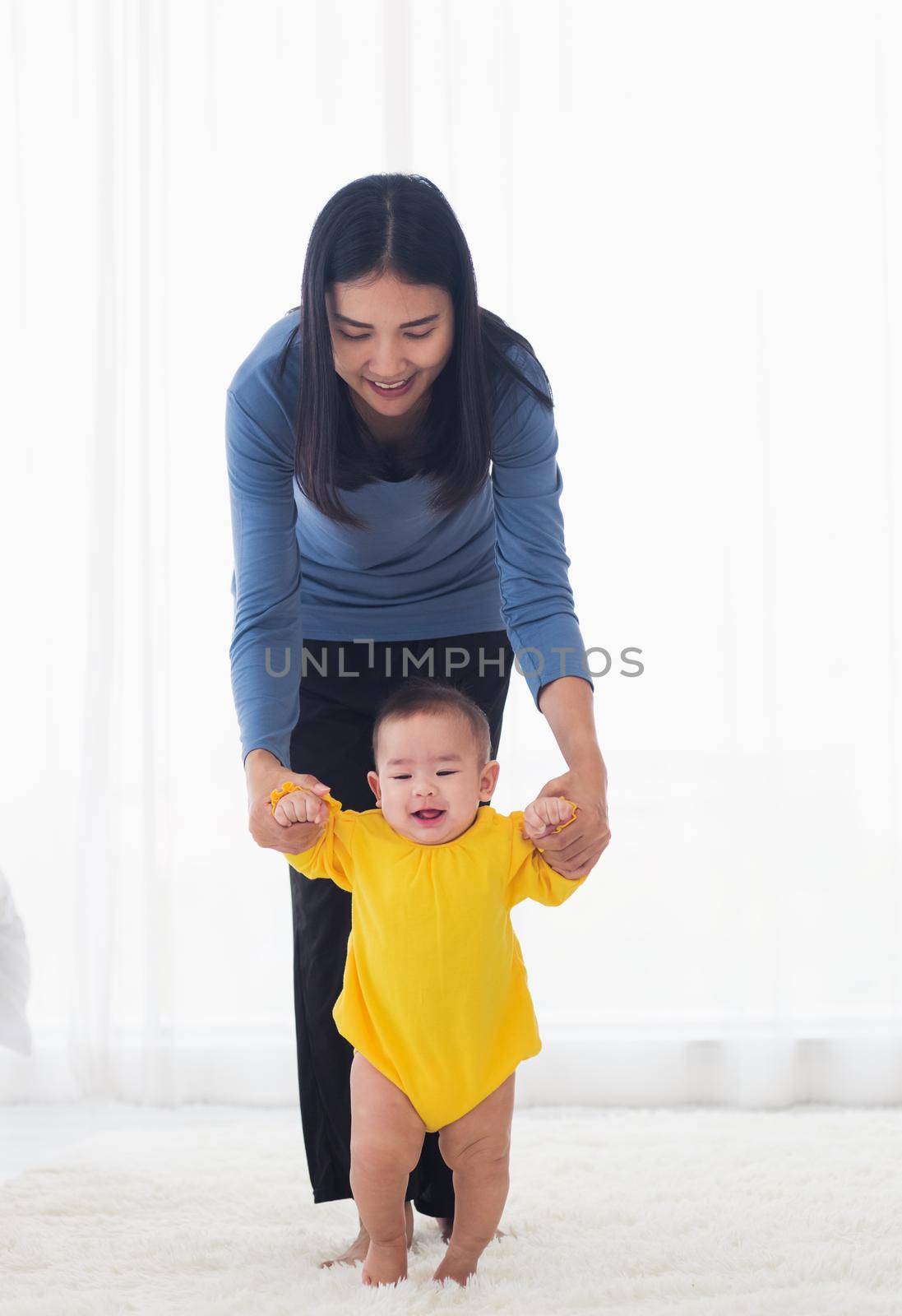 baby girl taking first steps learning to walk with mom by Sorapop