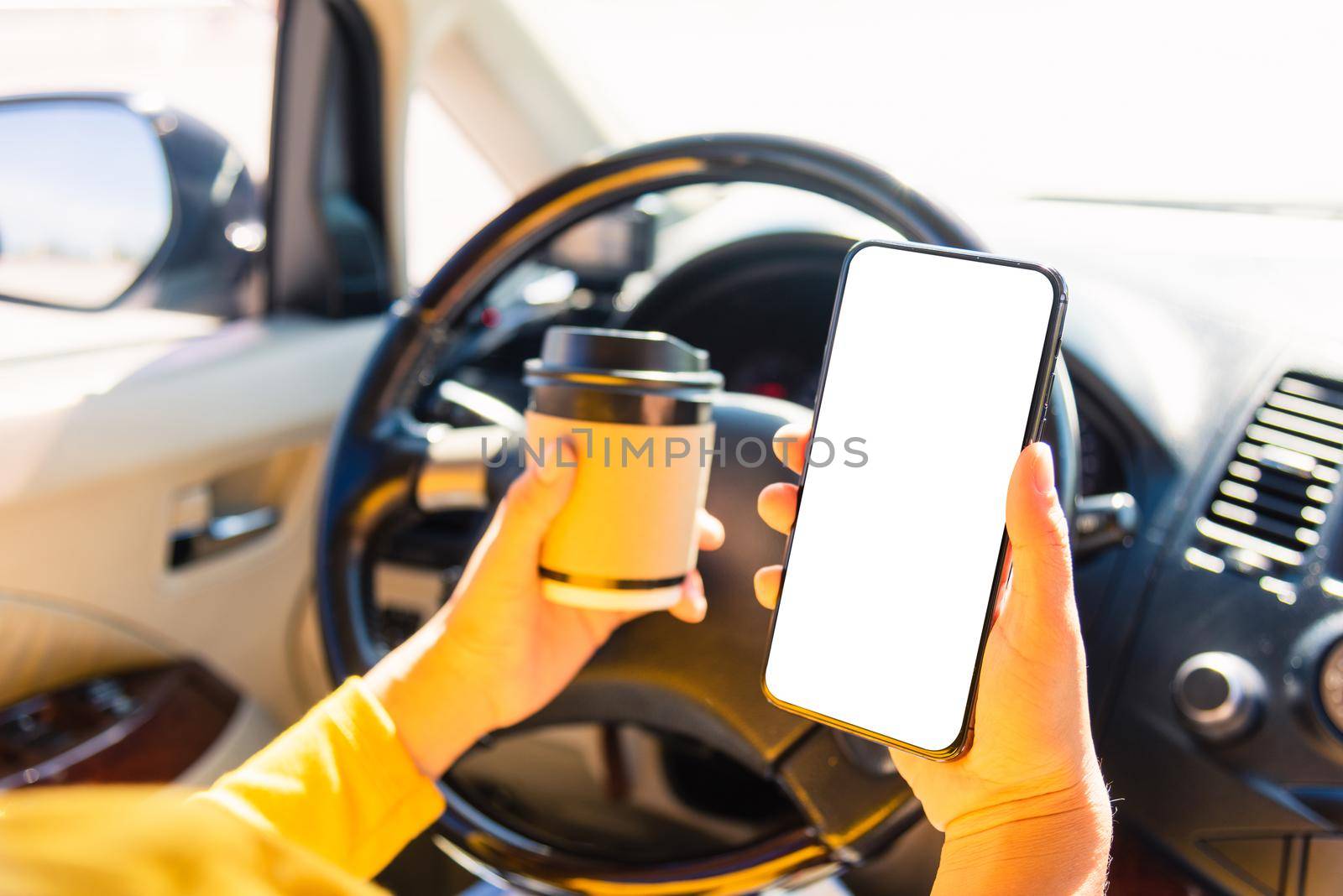 woman drinking hot coffee takeaway cup inside a car and using smartphone by Sorapop