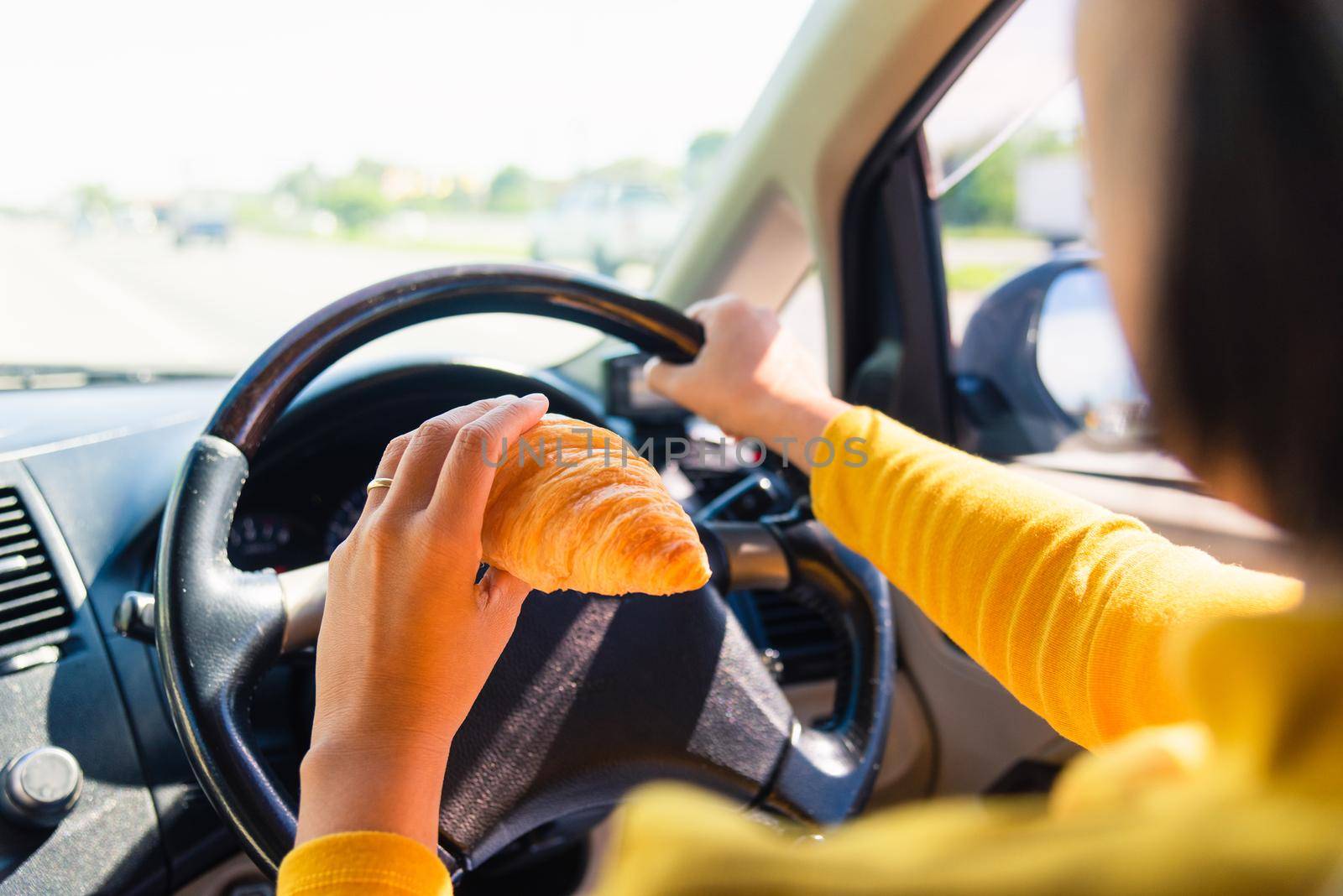 Asian woman eating food fastfood while driving the car in the morning during going to work on highway road, Transportation and vehicle concept