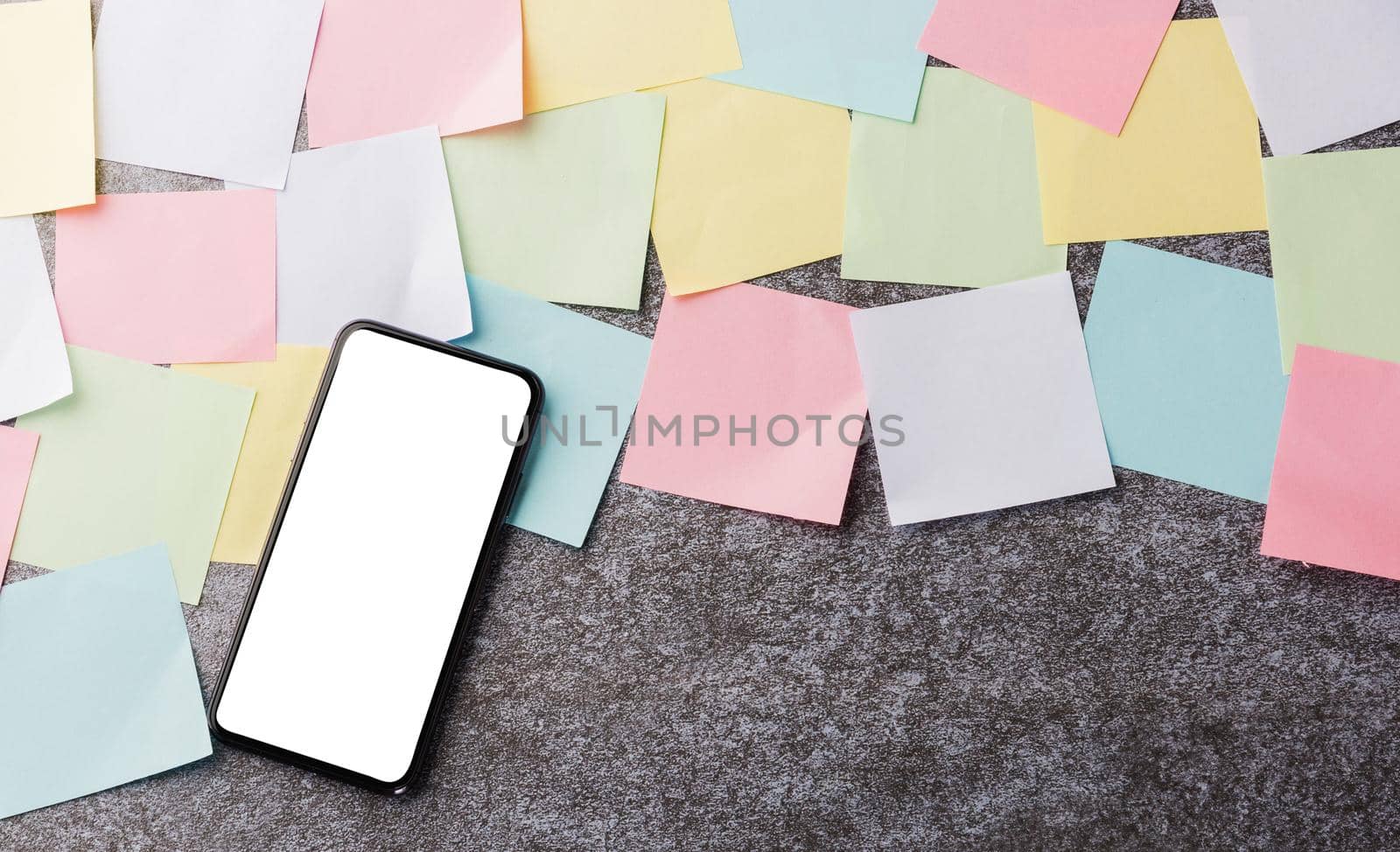 Above many blank paper stick note list with the modern black smart mobile phone blank screen on concrete background, Business smartphone reminder concept