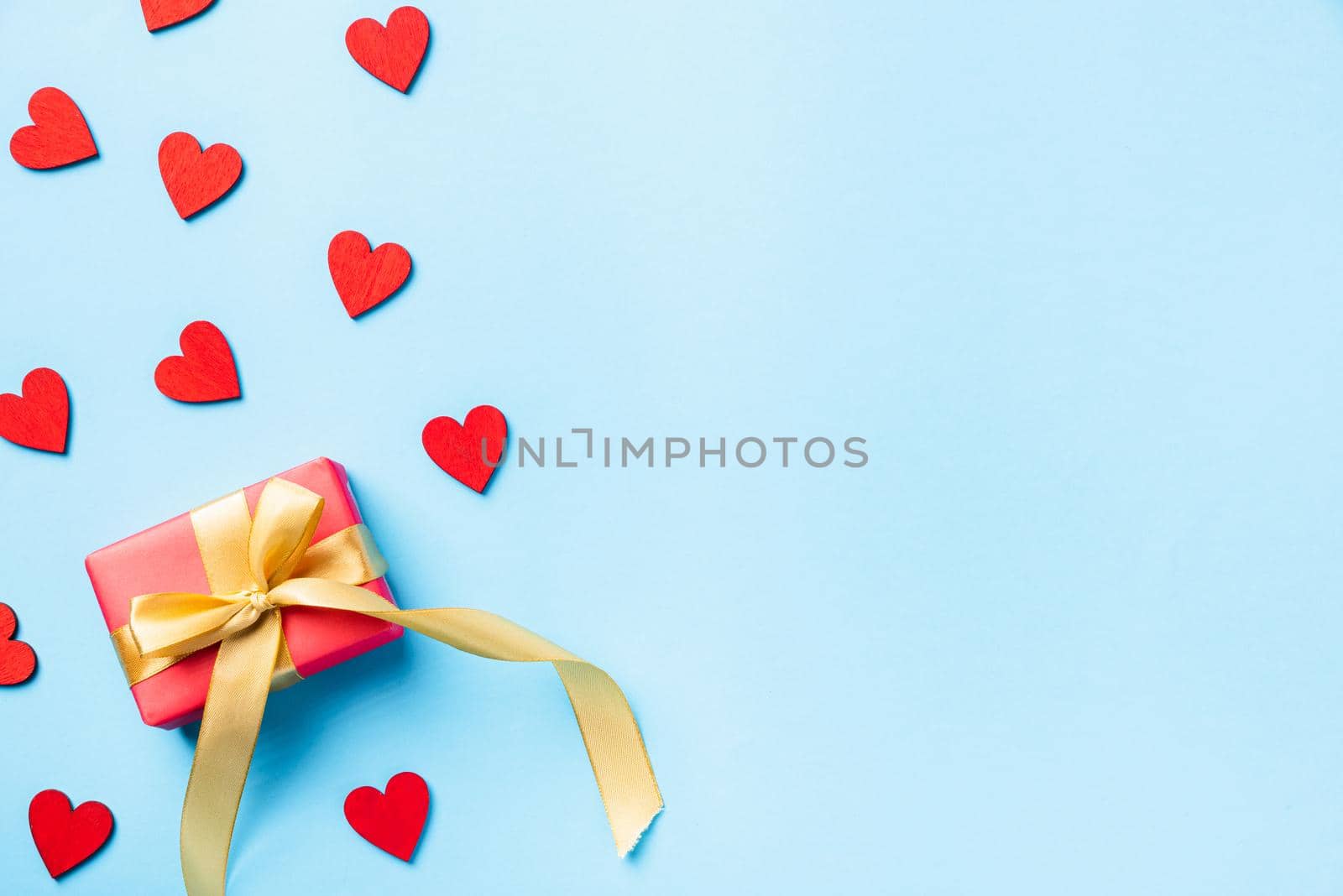 Happy Valentines' day background concept. Red gift box with a golden bow ribbon and wood red hearts composition greeting card for love isolated on blue background with copy space. Top View from above