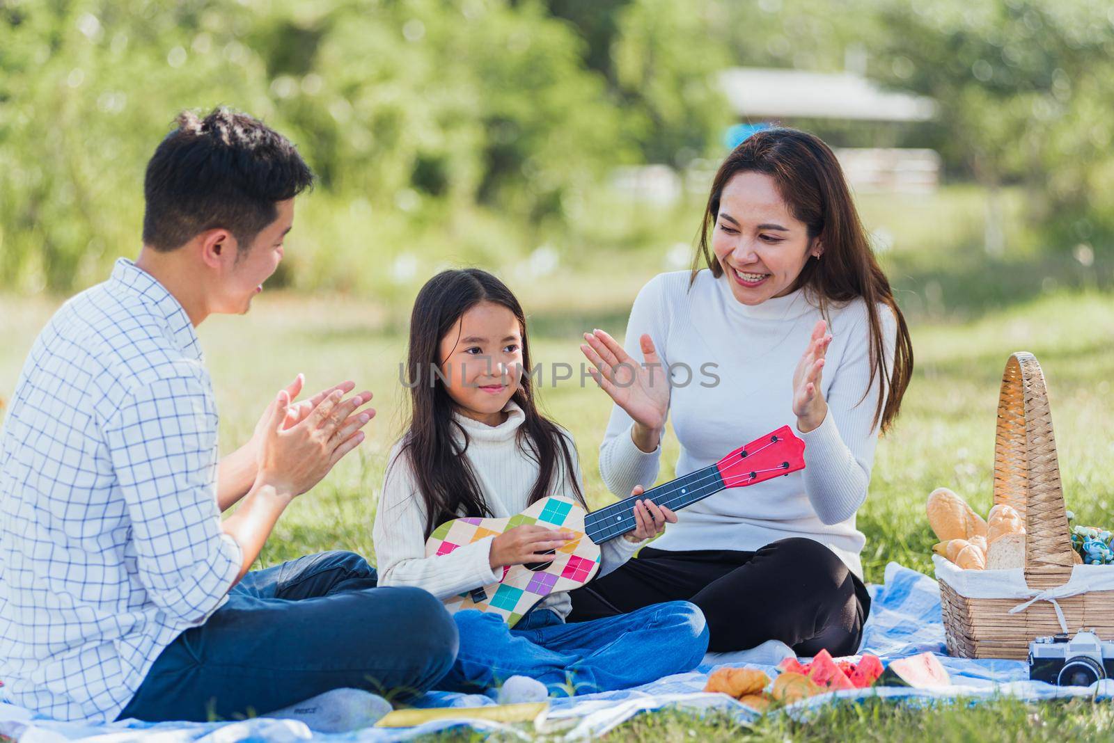 Happy family having fun and enjoying outdoor with playing Ukulele during a picnic by Sorapop