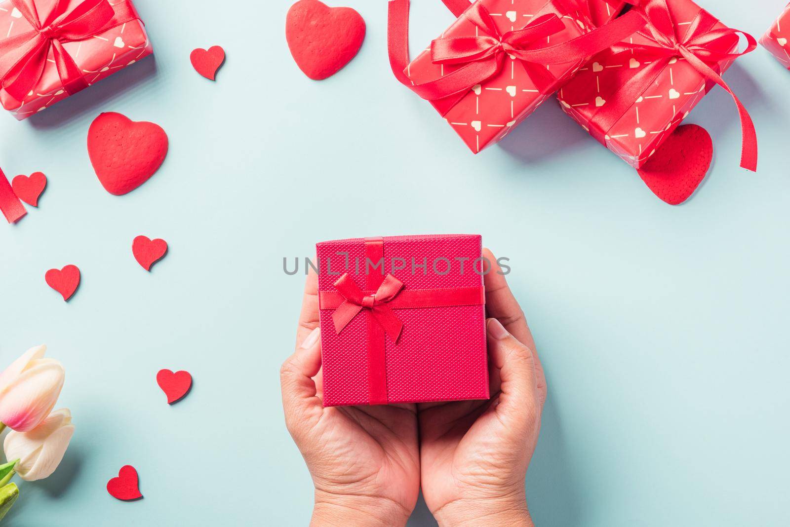 Valentine's day and birthday. Woman hands holding gift or present box decorated and red heart surprise on blue background, Female's hand hold gift box package in craft paper Top view flat lay