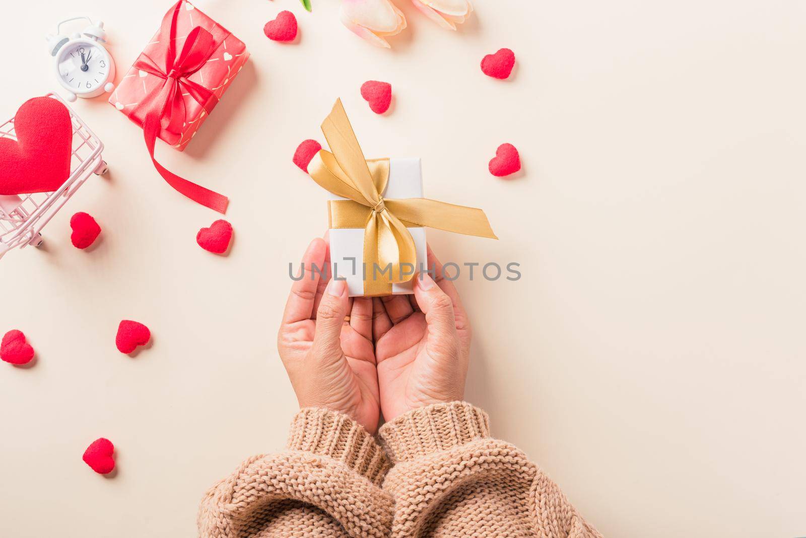 Valentine's day and birthday. Woman hands holding gift or present box decorated and red heart surprise on cream pastel background, Female's hand hold gift box package in craft paper Top view flat lay