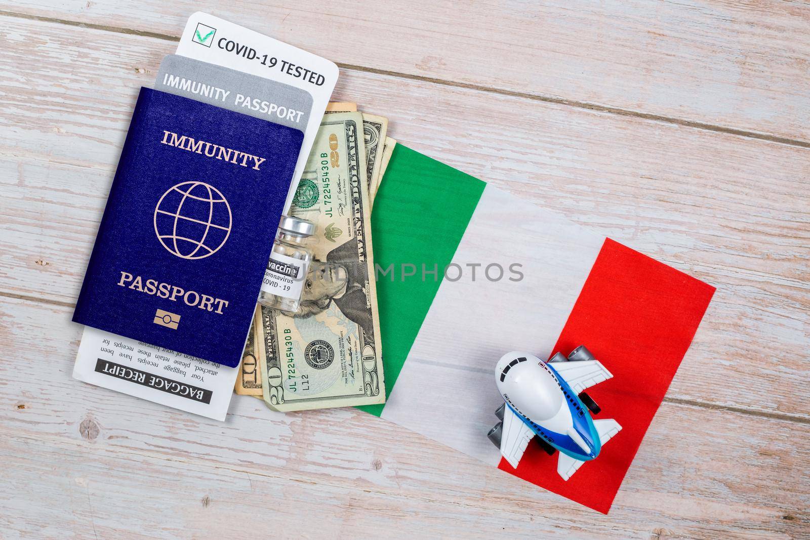 Concept of Immunity passport, certificate for traveling after pandemic for people who have had coronavirus or made vaccine. Passport with note COVID-19, banknotes, vaccine bottle on the flag of Italy