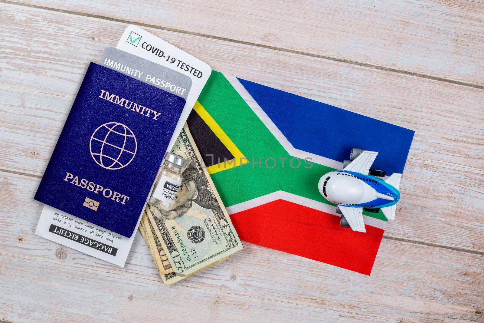 Concept of immunity to coronavirus. Certificate stating that person is not contagious. Passport with note covid-19 test passed, money, vaccine bottle and a toy plane on flag of South Africa