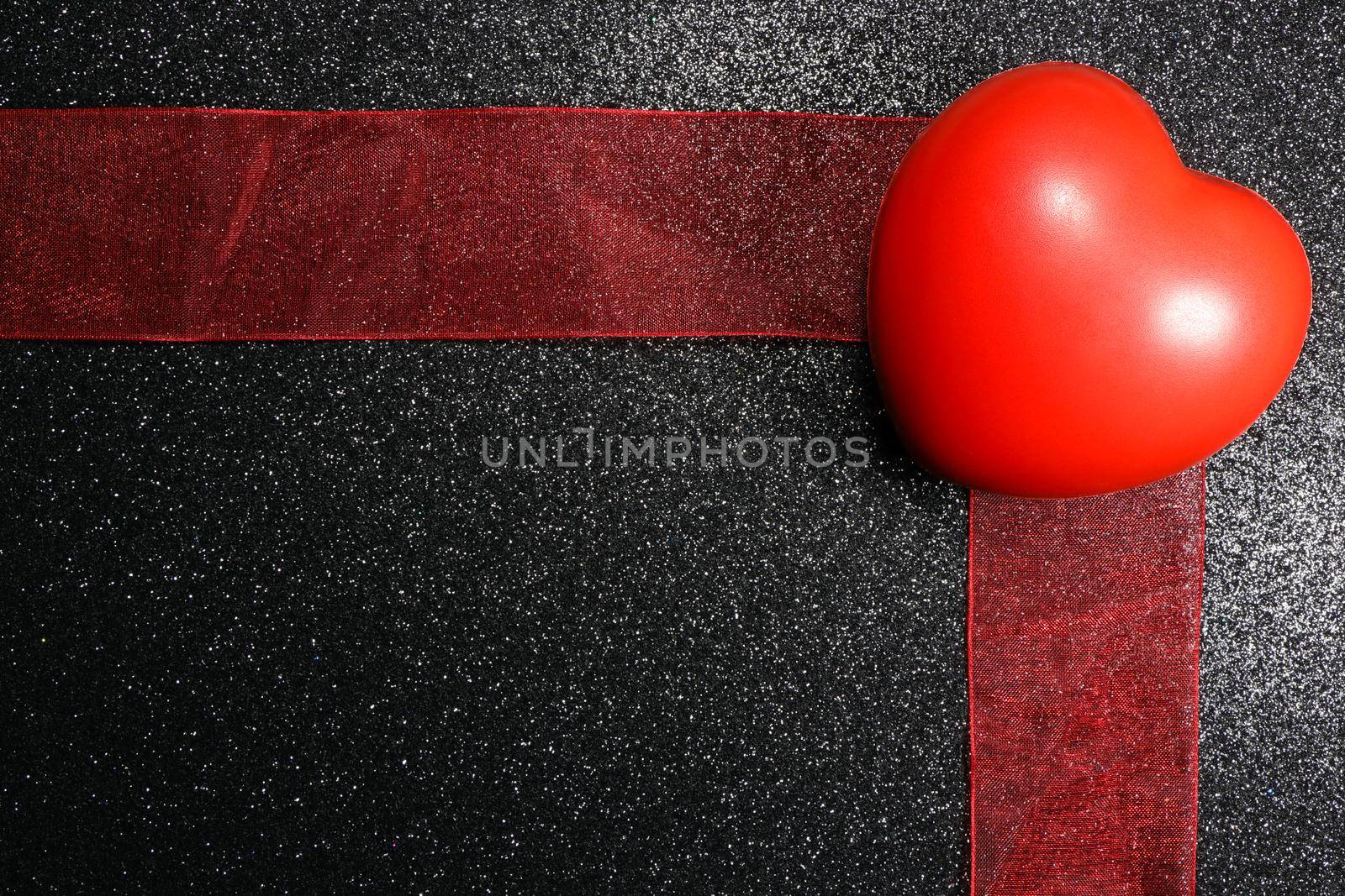 Saint Valentine's day big red heart toy and broad red ribbon on textured black background