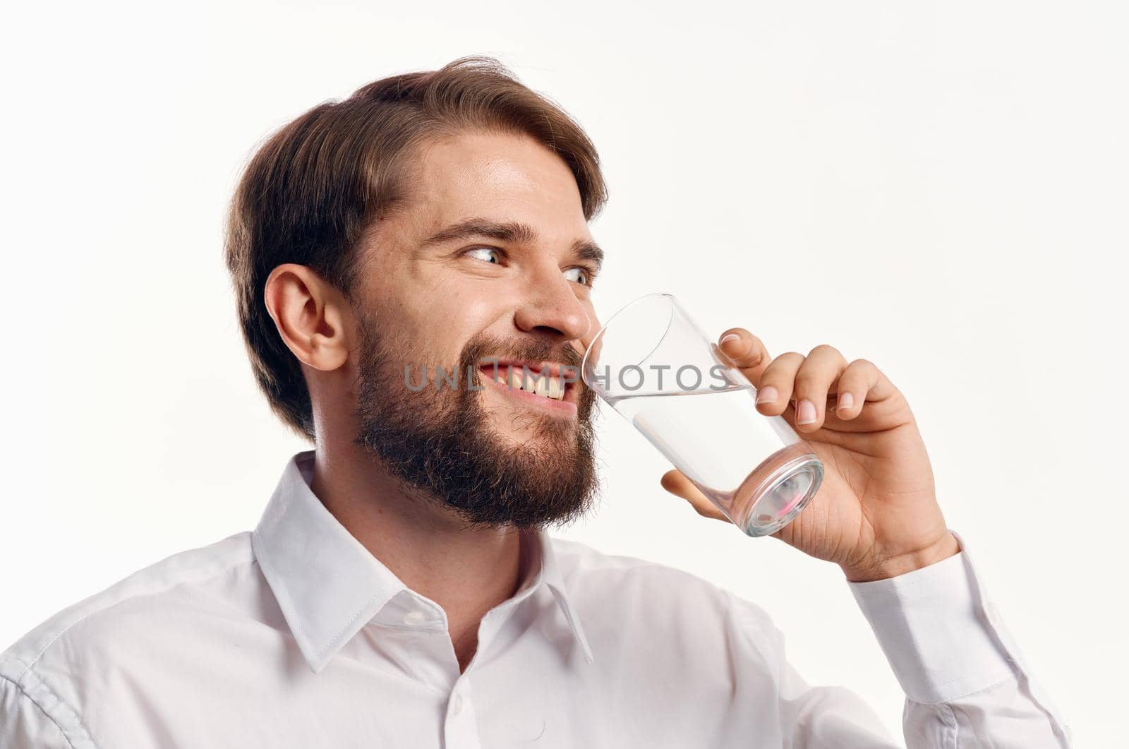 happy man drinks water from a glass on a light background white shirt portrait model. High quality photo