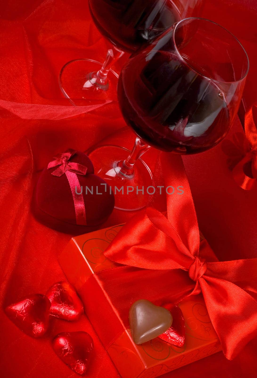 Valentine's Day. Gift box, flowers, glasses with wine and candy in the form of a heart on a red background by aprilphoto