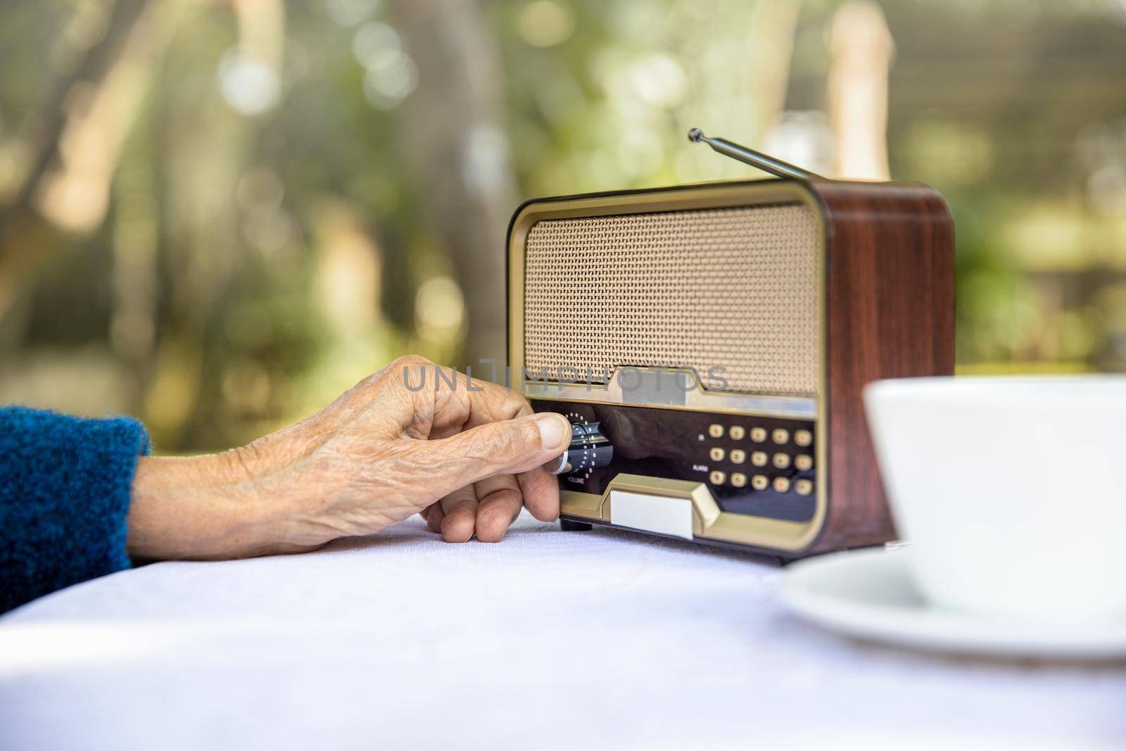 Senior woman hand turning knob on vintage radio in backyard. by toa55