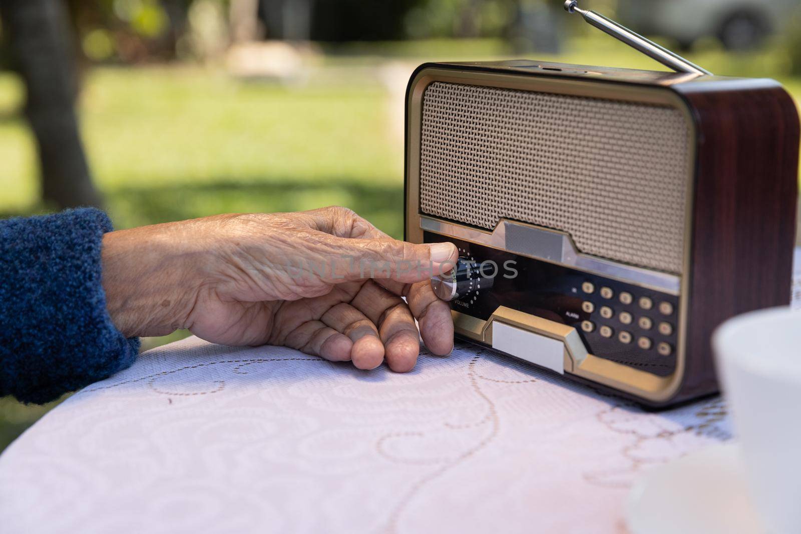 Senior woman hand turning knob on vintage radio in backyard.