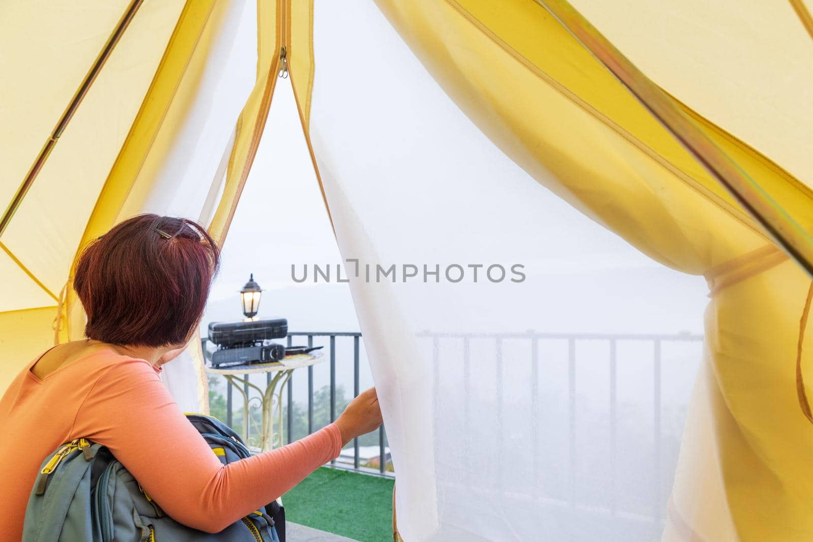 Middle aged woman sitting inside yellow tent looking at valley