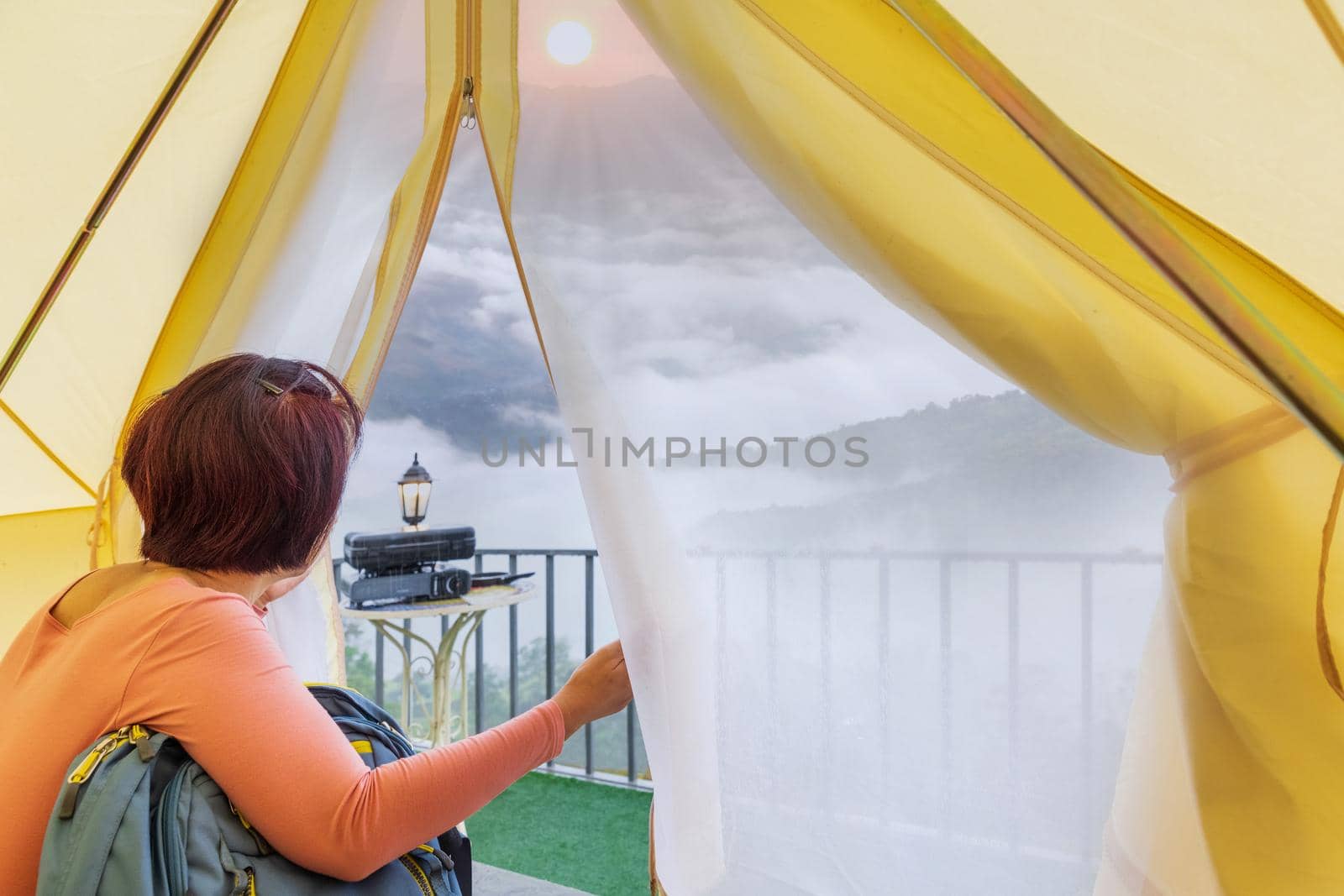 Middle aged woman sitting inside yellow tent looking at valley