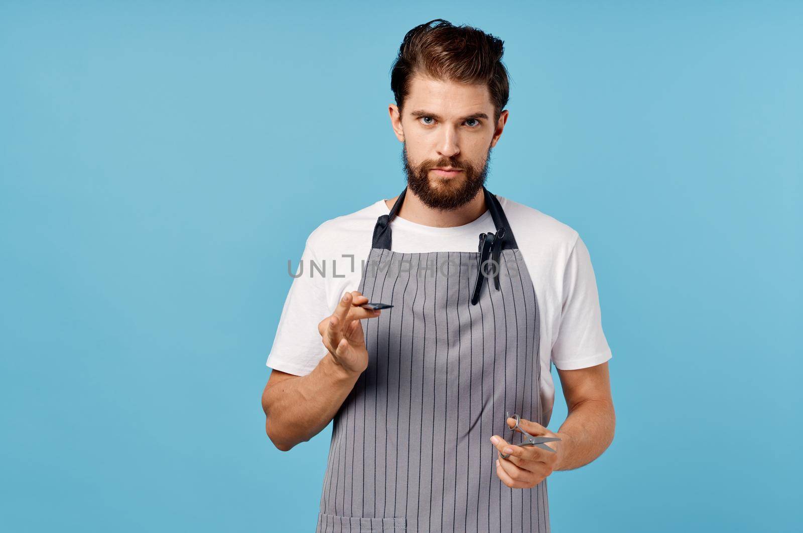 a man hairdresser in a gray apron does his hair on a blue background scissors comb. High quality photo