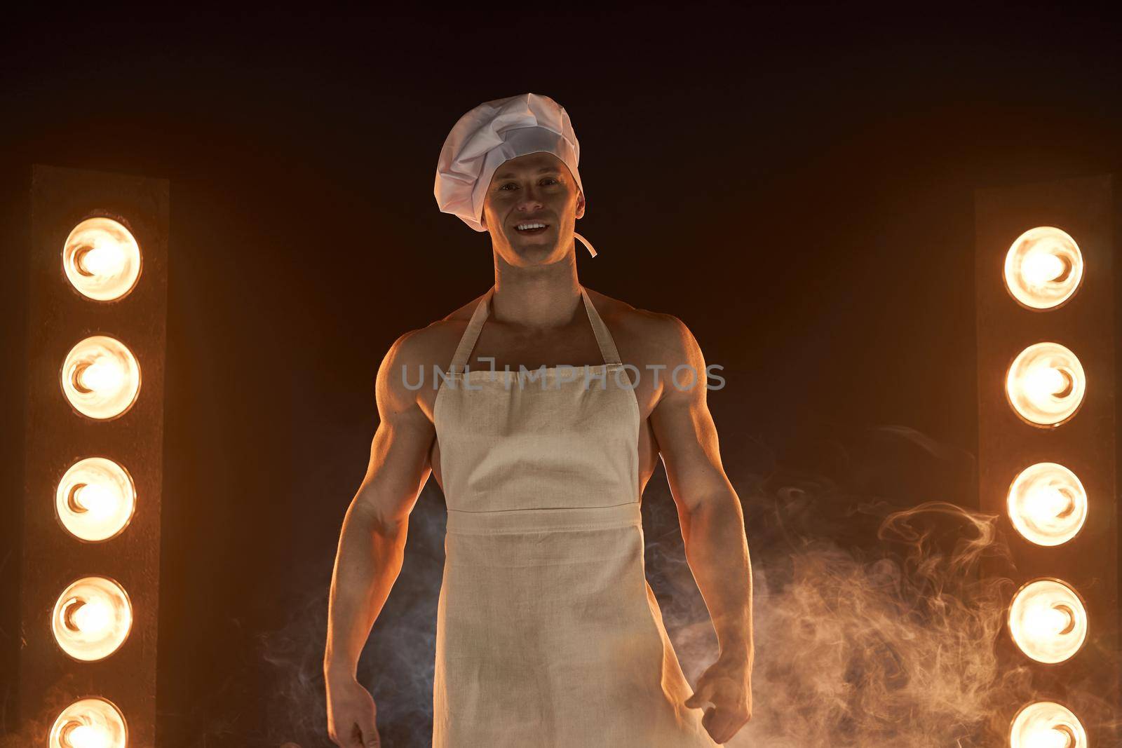 Portrait of muscular chef wearing white apron and cheef hat, posing on smoky background male housewife. husband in kitchen. brutal butcher.