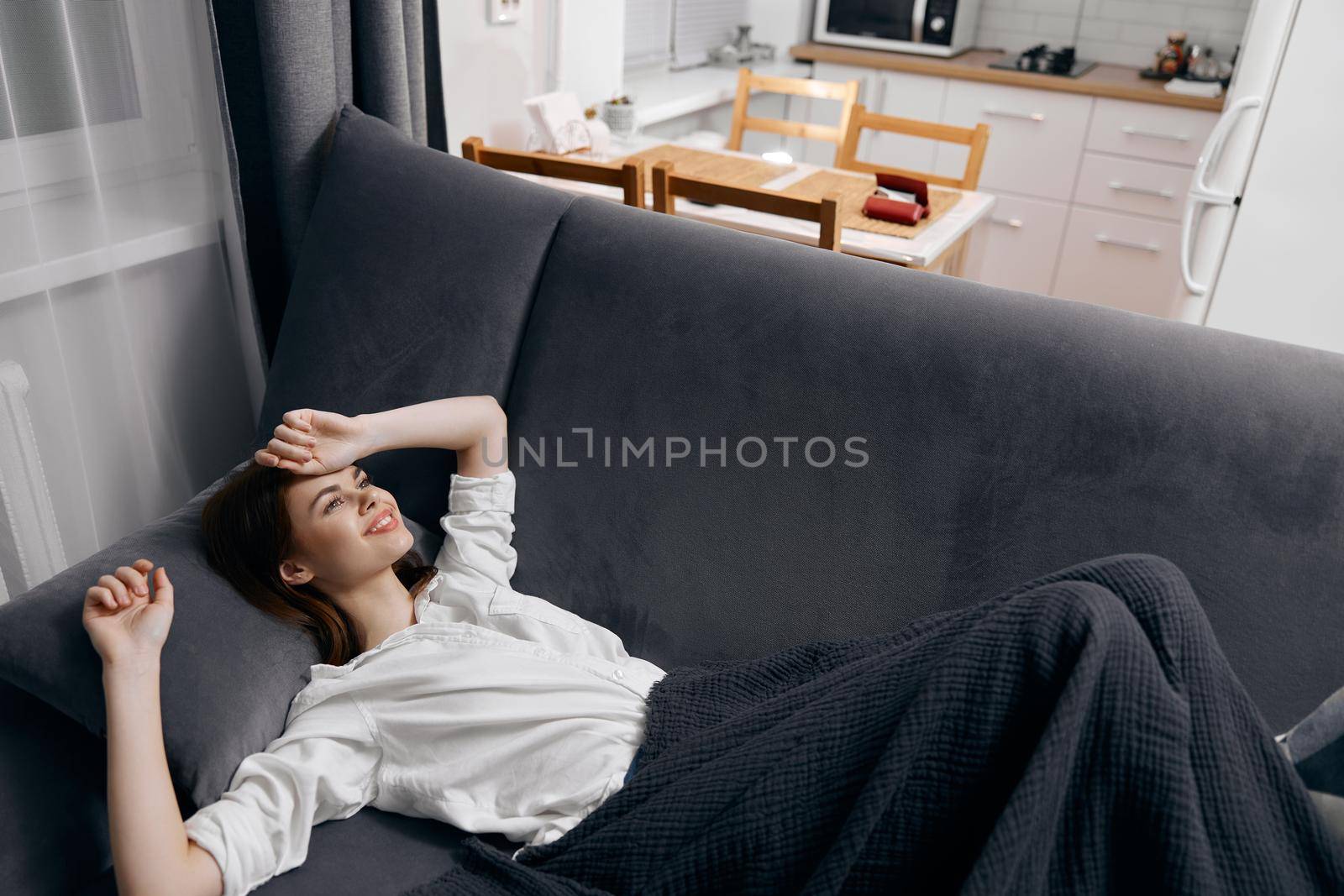 woman covered with a blanket is lying on the sofa and looking up the window in the background. High quality photo
