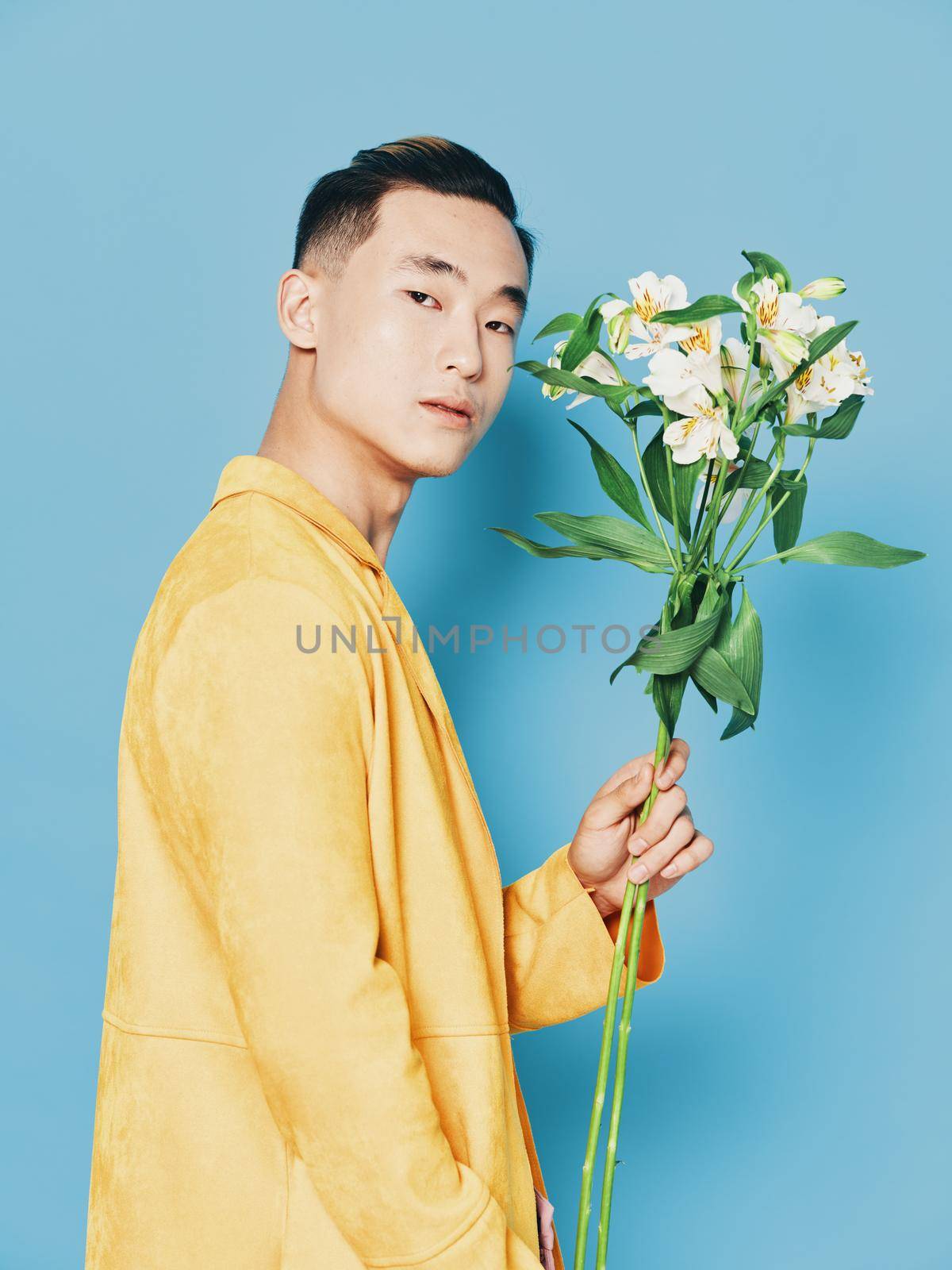 Side view of a guy with a bouquet of flowers in a yellow coat on a blue background. High quality photo