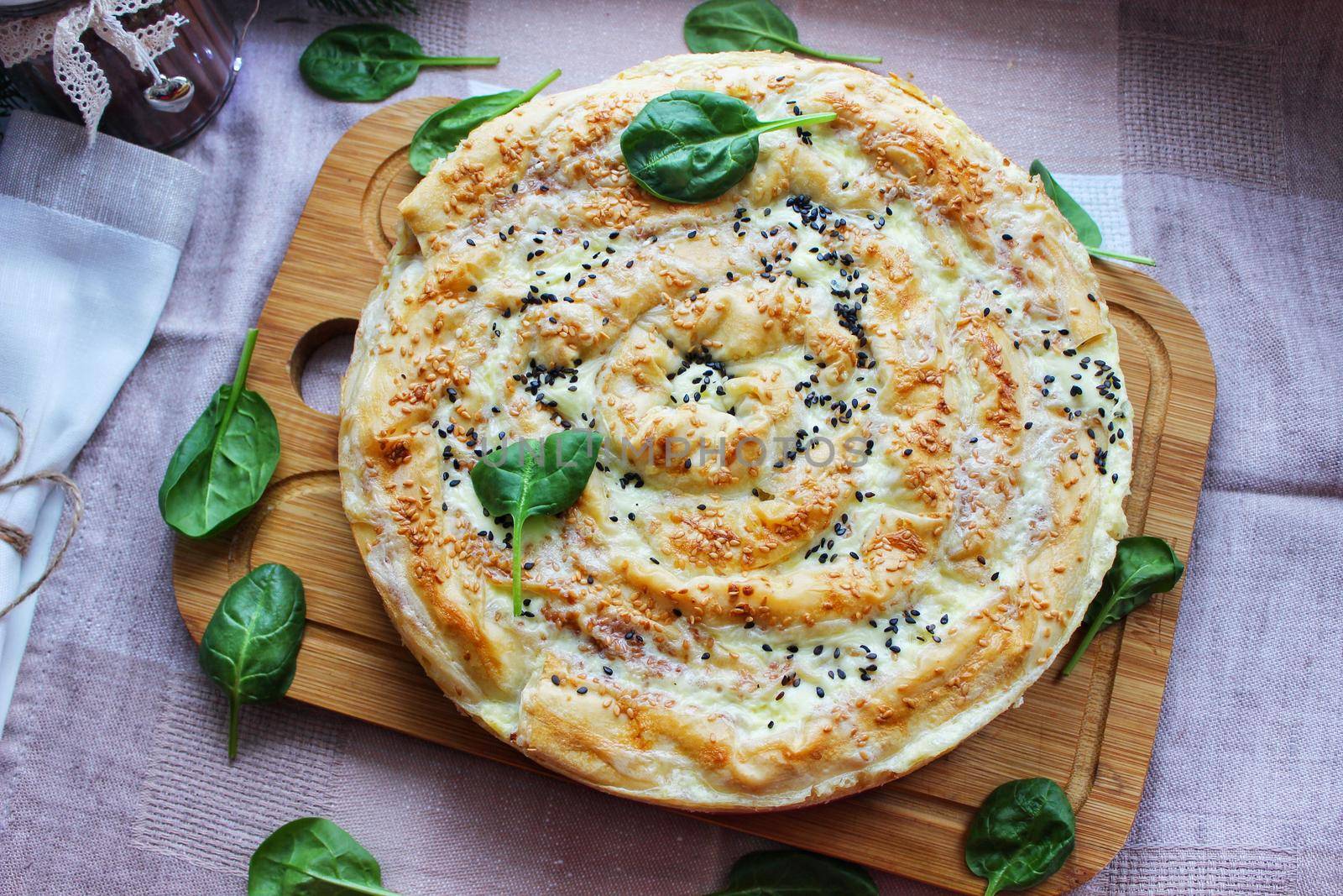 Large round piece of baked lasagna on a wooden chopping board close up.Texture or background