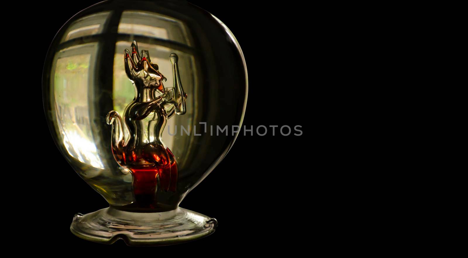 A bottle with a glass figure of a devil with red elements inside. Halloween festival concept. Black background with place for text by mtx
