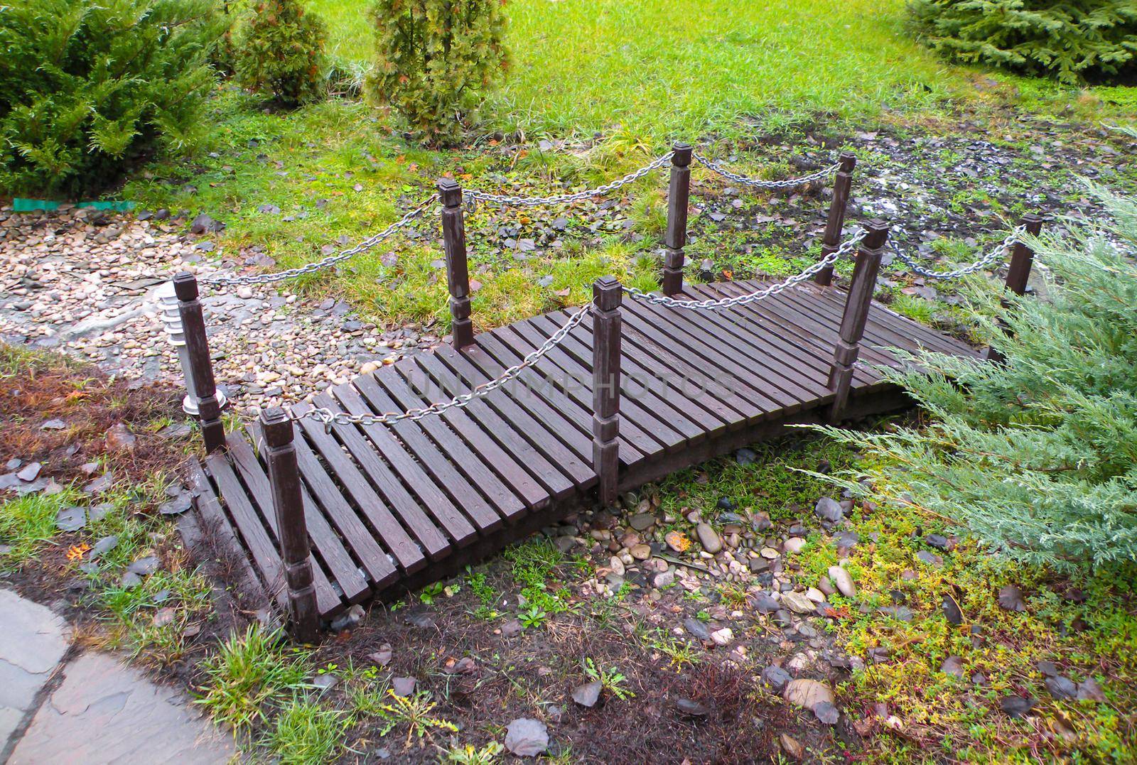 A small wooden bridge made of brown wood in the garden. A bridge over a stream in stones.