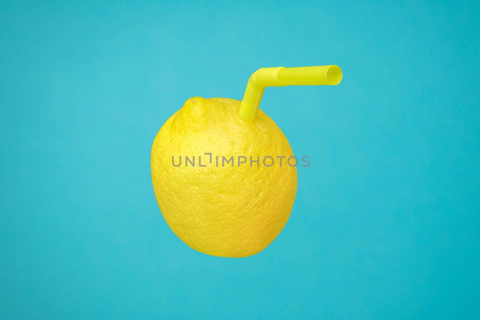 Ripe juicy lemon as a drink in glass with straw or natural freshly lemonade made with real fruit on blue. Vitamin C in yellow lemon fruit minimal concept or homemade lemonade squeezed refreshing drink by synel