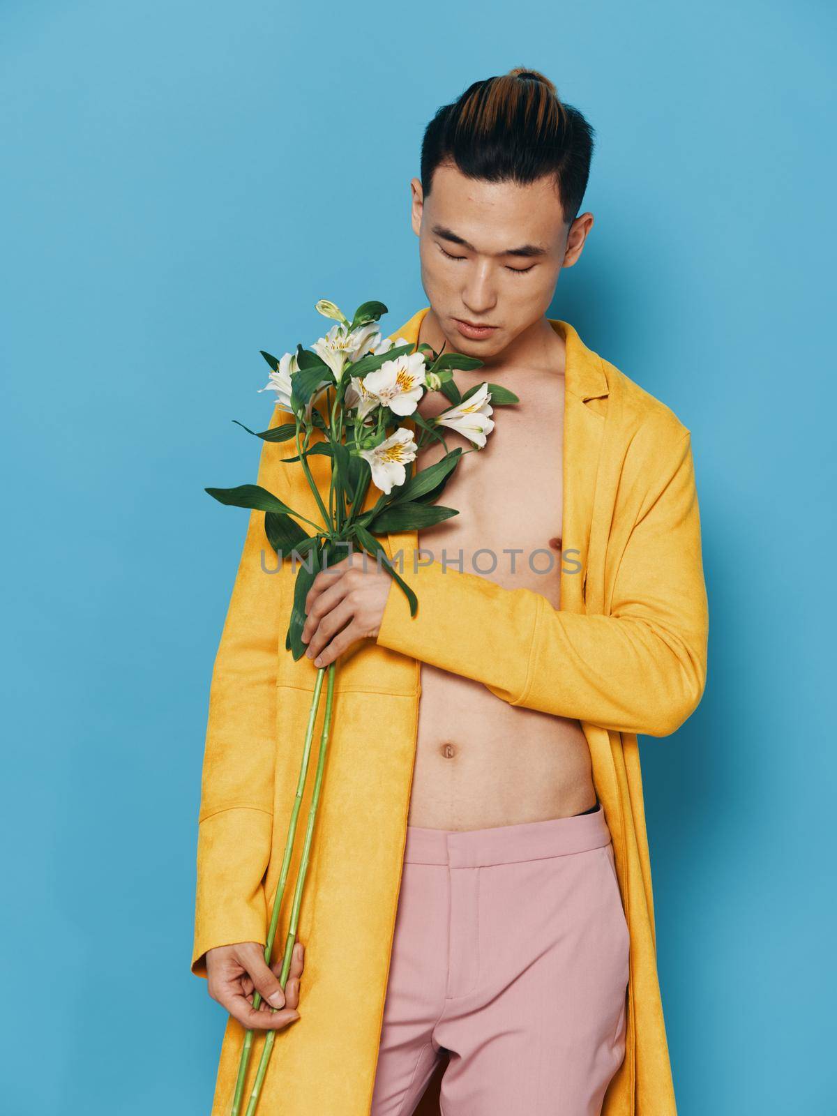 Portrait of a man of Asian appearance on a blue background with a bouquet of white flowers and a yellow coat. High quality photo