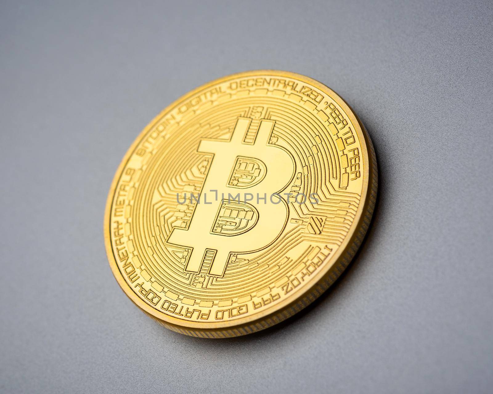 Physical cryptocurrency golden Bitcoin coin on brushed aluminium background.