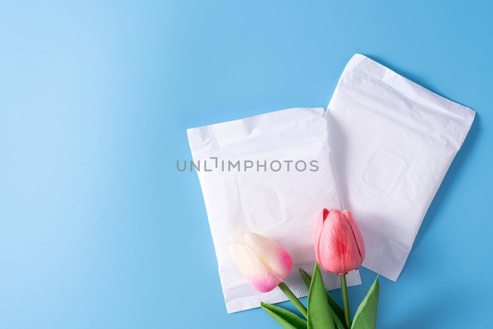 Sanitary pad, Sanitary napkin with tulip flower on blue background. Menstruation, Feminine hygiene, top view.