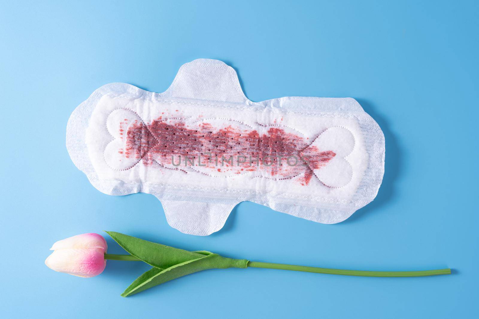 Used Sanitary pad with full amount of blood, Sanitary napkin with tulip flower on blue background. Menstruation, Feminine hygiene, top view.