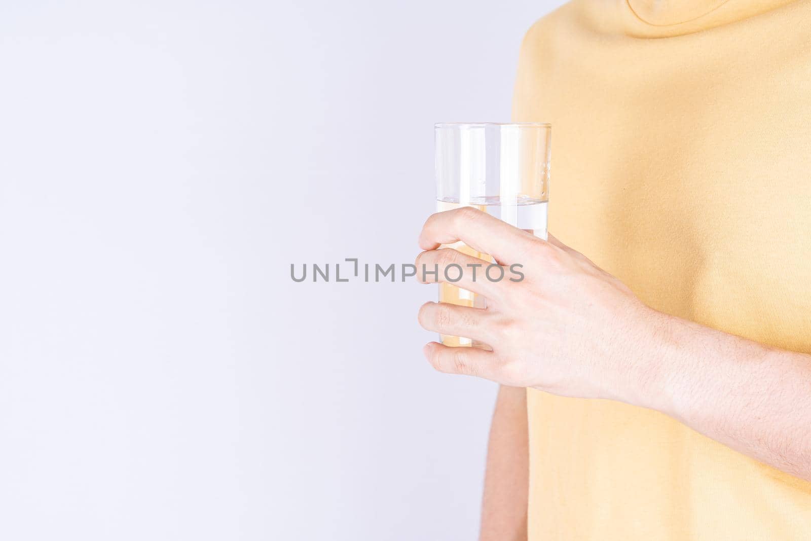 Man holding glass of water isolated grey background. Clean drinking water in clear glass.