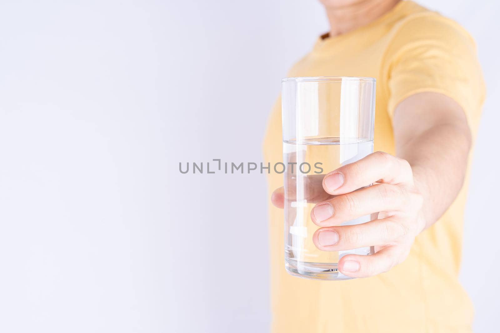 Man holding glass of water isolated grey background. Clean drinking water in clear glass.