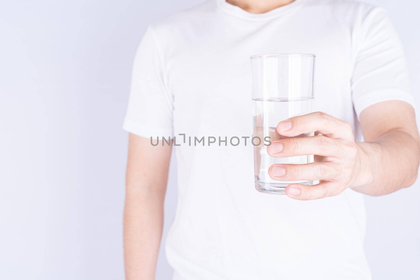 Man holding glass of water isolated grey background. Clean drinking water in clear glass.