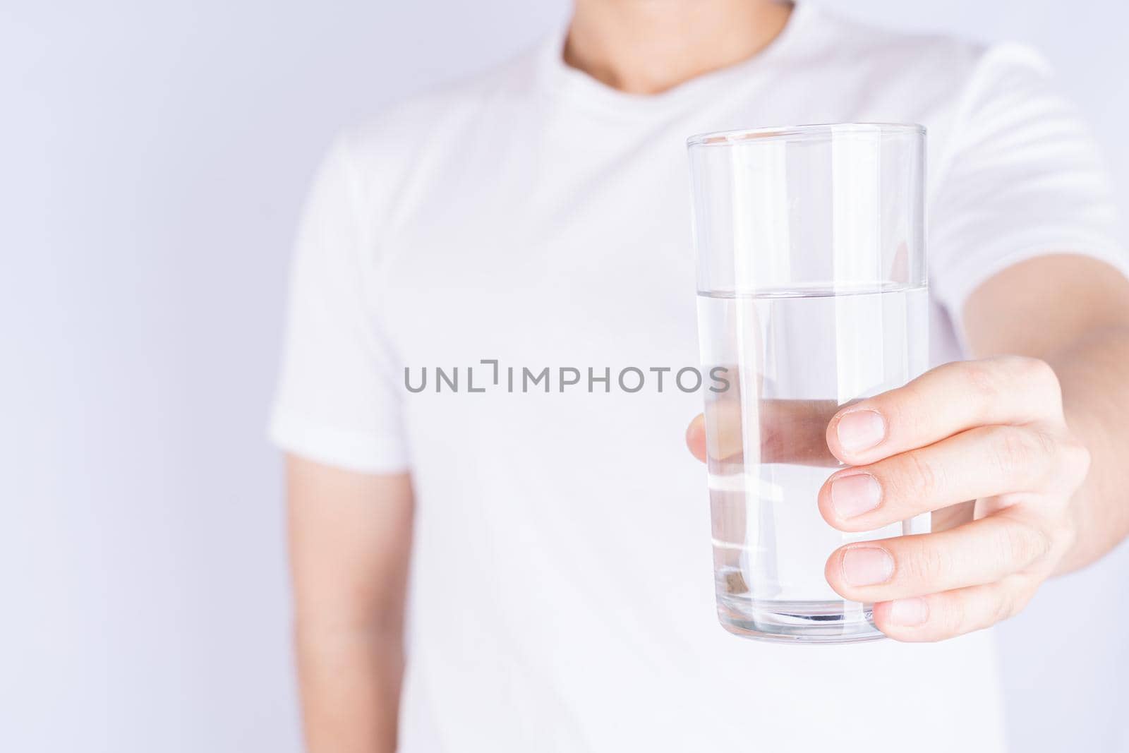Man holding glass of water isolated grey background. Clean drinking water in clear glass.