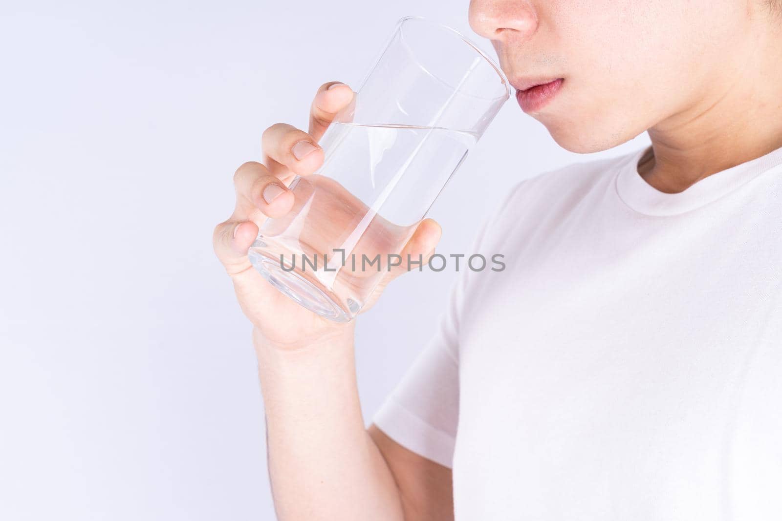 Man drinking water isolated grey background. Clean drinking water in clear glass.