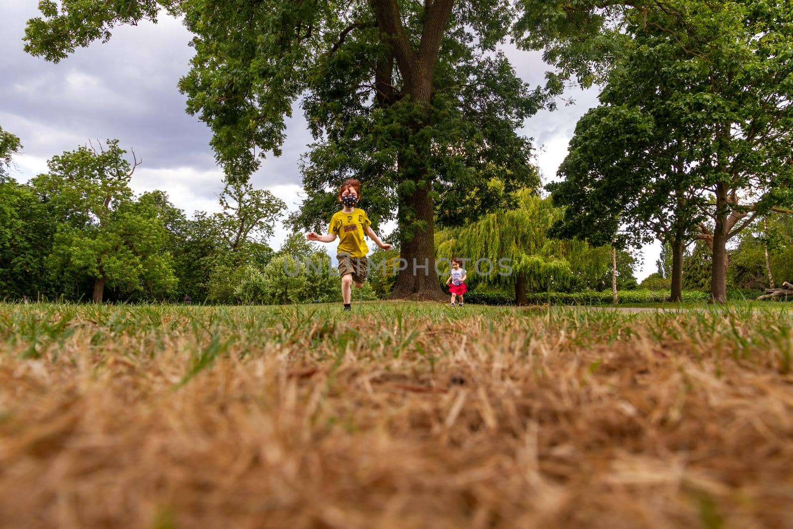 boy and a girl running in a park towards the camera on a sunny summer day wearing a face mask