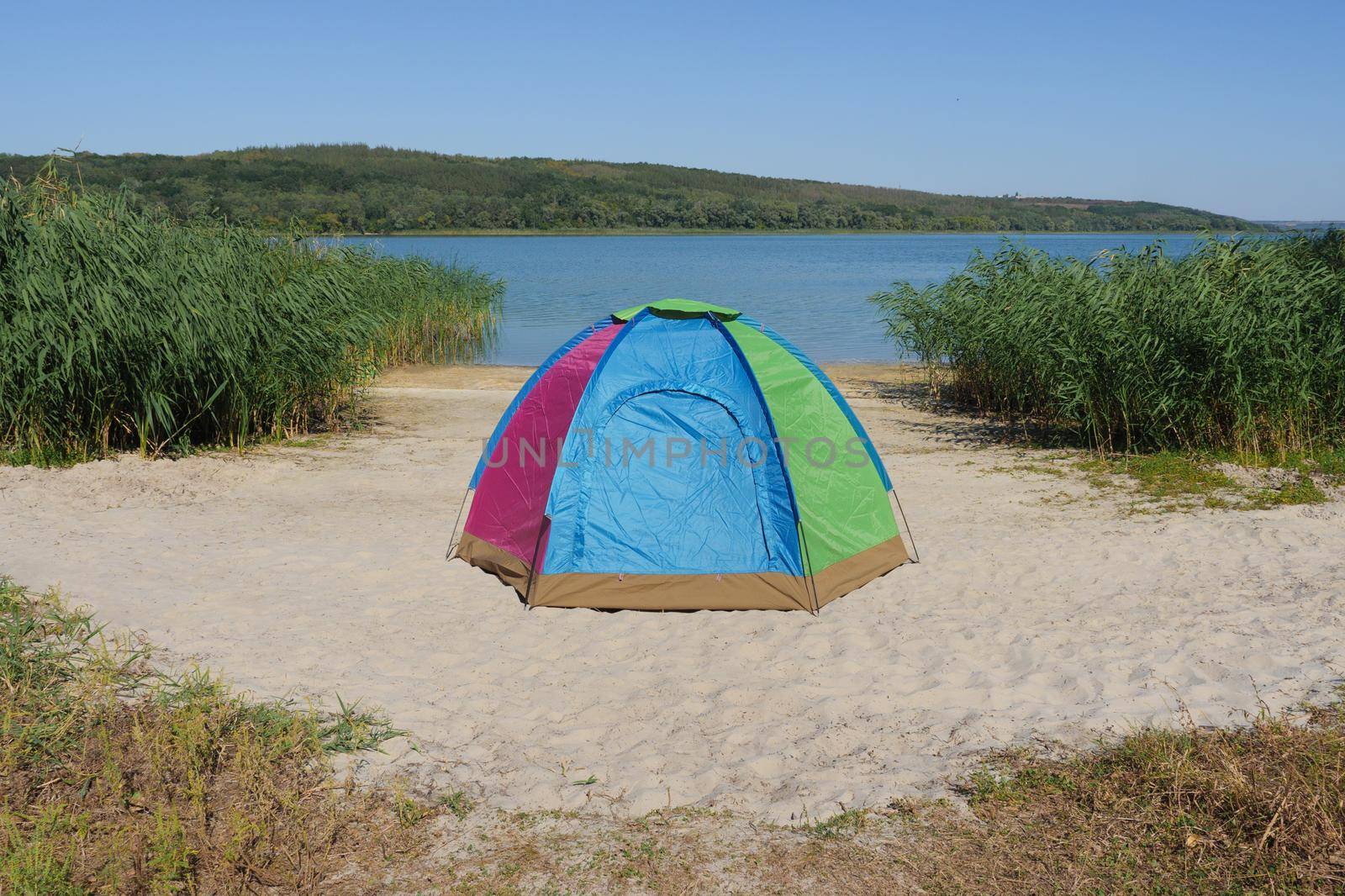 Tourist tent for trekking eco travel or fishing. Colourful dome tent on lake shore or camping equipment travel. Nobody near camping tent located on sand bank river in local hike travel solitude nature by synel