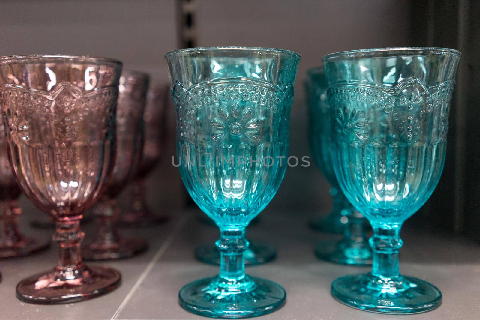 High notched wine glasses colored glass, standing on a shelf.