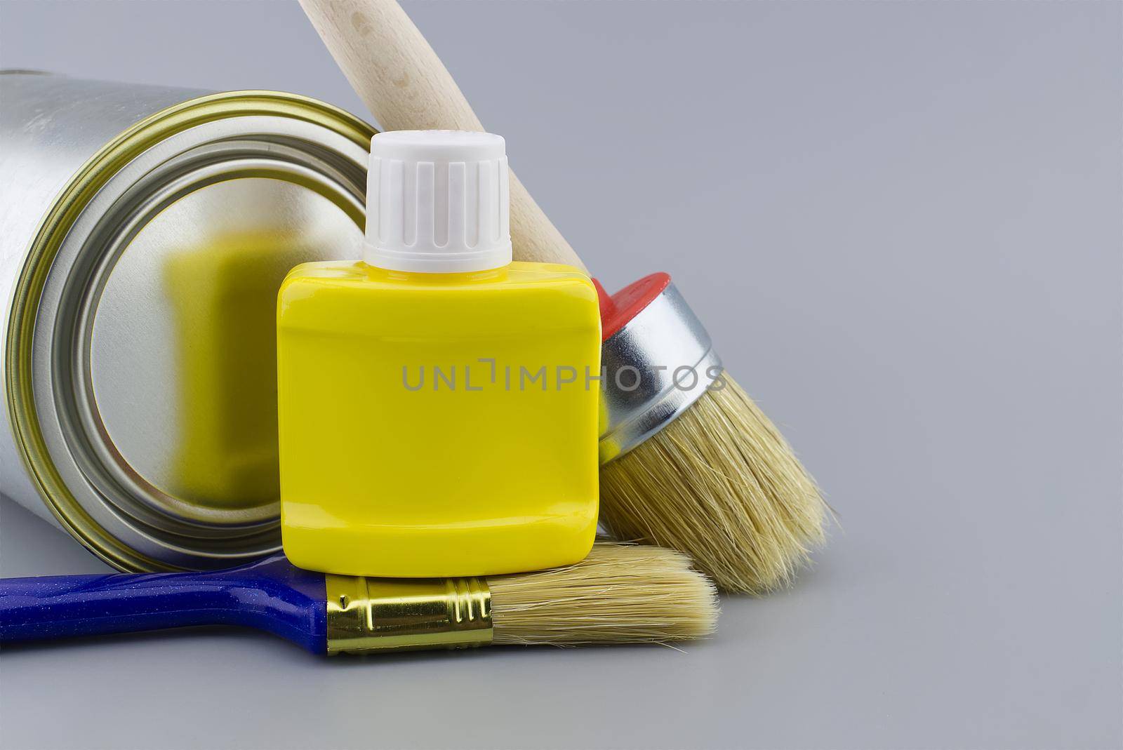 DIY, decorating or renovations concept with a still life with assorted clean paint brushes and unlabeled tin of paint over a grey background
