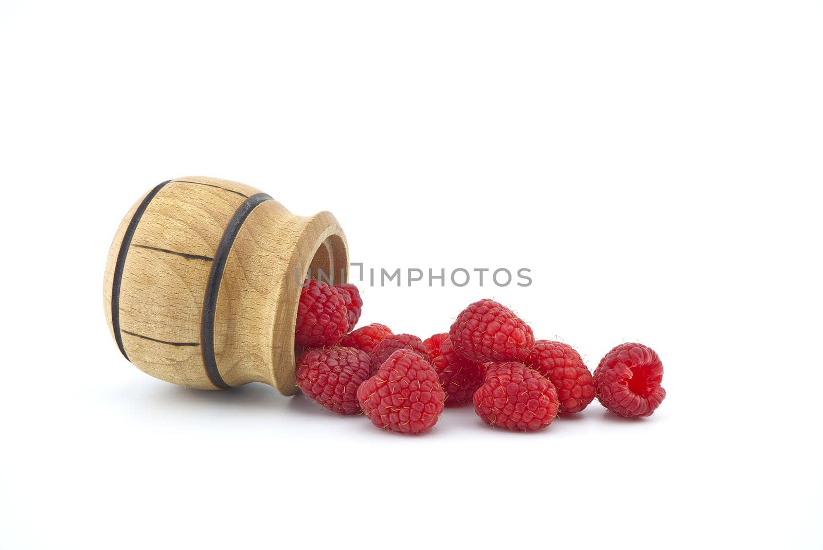 Heap of red ripe raspberry berries fall out of a wooden container isolated on white background