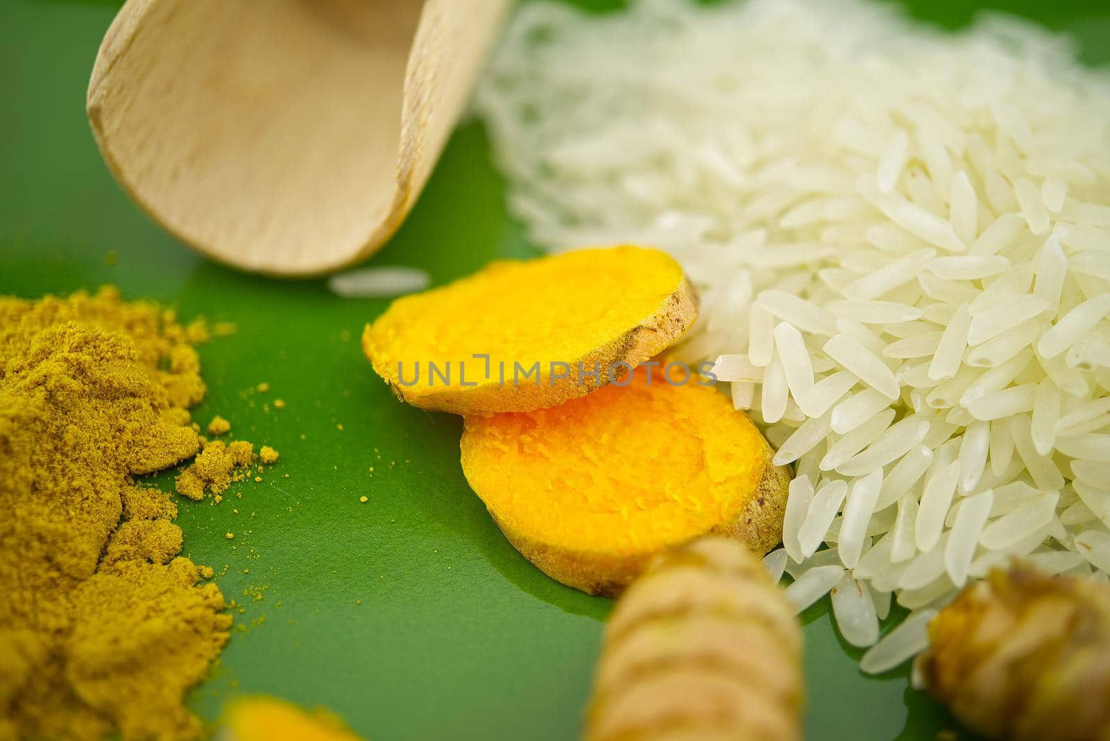 Turmeric roots and slices next to heaps of rice and spice powder on a green plate. Selective focus and free space for text