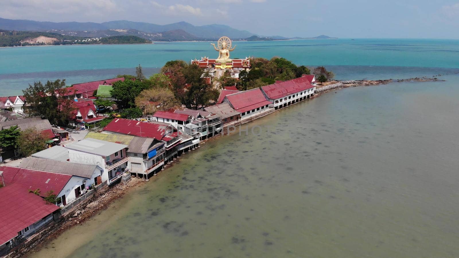 Island with Buddhist temple and many houses. Aerial view of island with Buddhist temple with statue Big Buddha surrounded by traditional houses on stilts in bay of Pacific ocean on Samui, Thailand. by DogoraSun