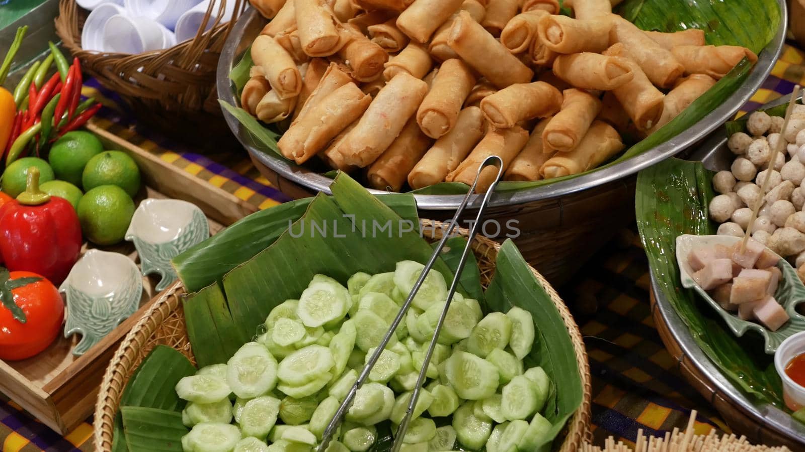 Bowls with traditional Asian dishes for sale. Bowls with fresh vegetables and fried spring rolls placed on stall of traditional street diner in Thailand