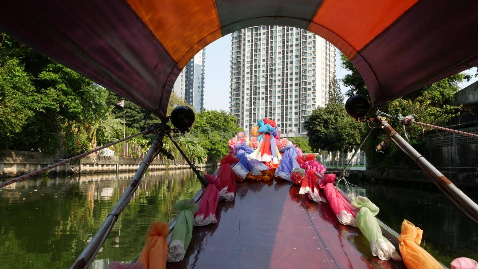 Tourist trip on Asian canal. View of calm channel and residential houses from decorated traditional Thai boat during tourist trip in Bangkok. by DogoraSun