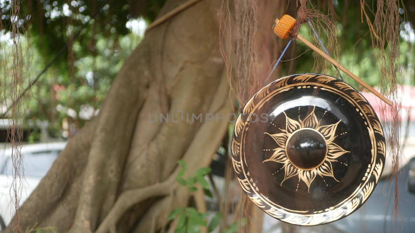 Small traditional gong hanging on background of old banyan tree in daylight. Symbol of buddhist religion. Tropical idyllic natural background. Zen meditation, retreat and enlightenment concept. by DogoraSun