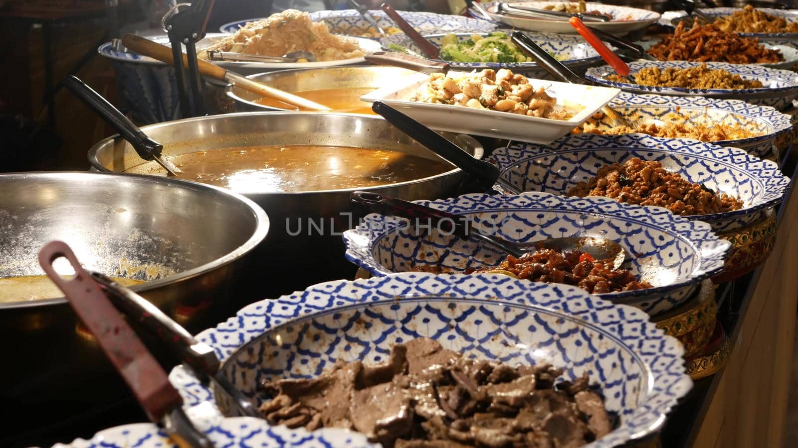 Bowls with various Asian dishes on stall. Bowls of assorted traditional Thai dishes placed on stall of street diner in evening. Oriental night market food court