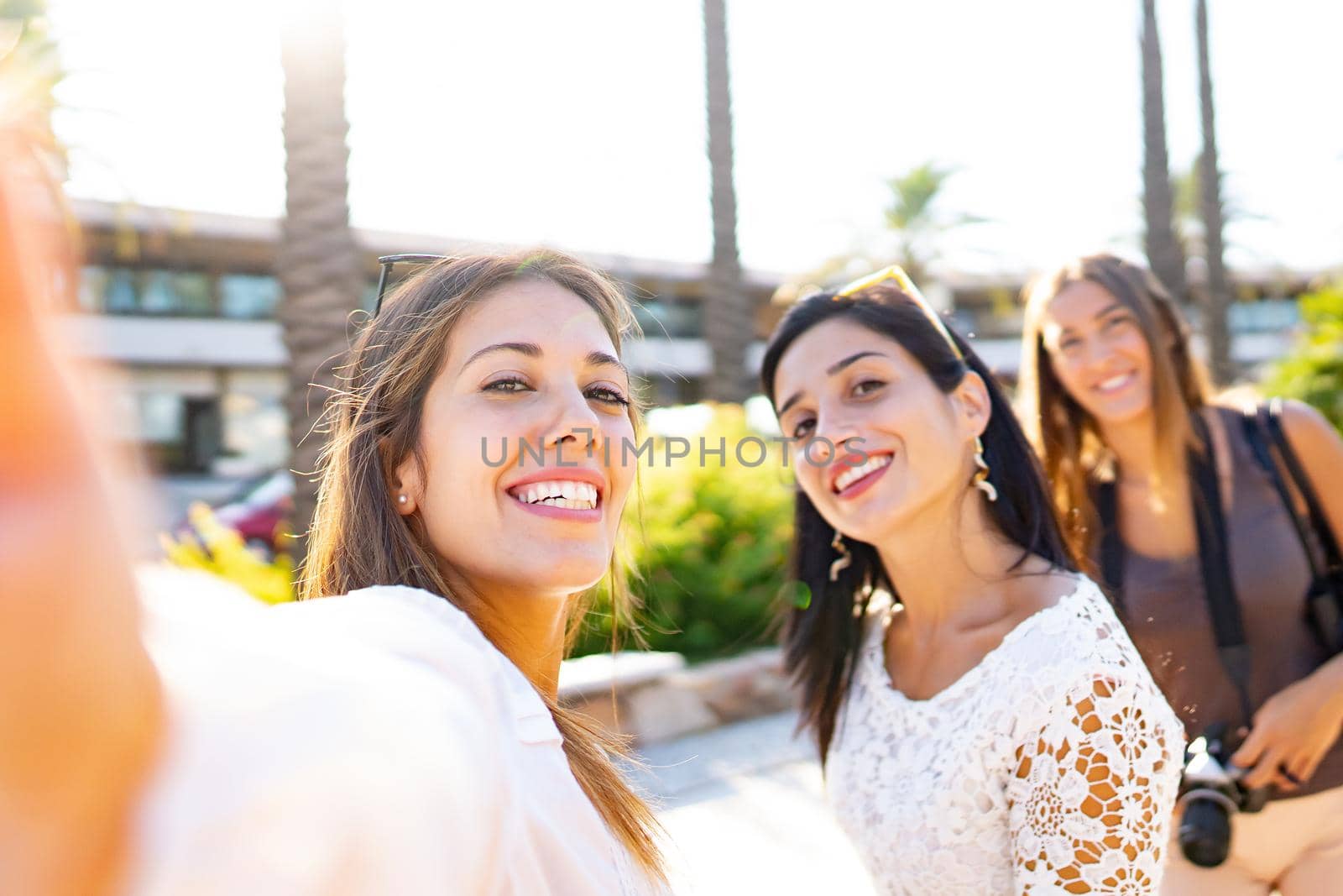 Three happy girls on vacation taking selfies in the city smiling looking at the camera. Beautiful young women having fun with technology and photography outdoor in the city enjoying travel destination