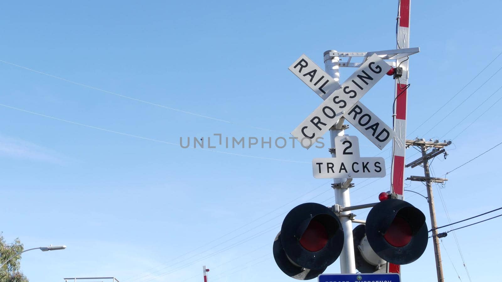 Level crossing warning signal in USA. Crossbuck notice and red traffic light on rail road intersection in California. Railway transportation safety symbol. Caution sign about hazard and train track.